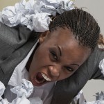 African business woman is tired of work . Sitting in front of crumpled paper pile . Unhappy with cv